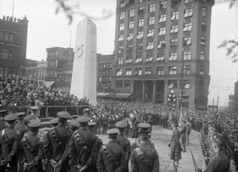 An old photo shows thousands of people gathered around a large obelisk. Many are in early 20th Century military uniforms.