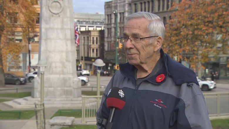 A man wearing a poppy stands in front of the Victory Square Cenotaph in Vancouver.