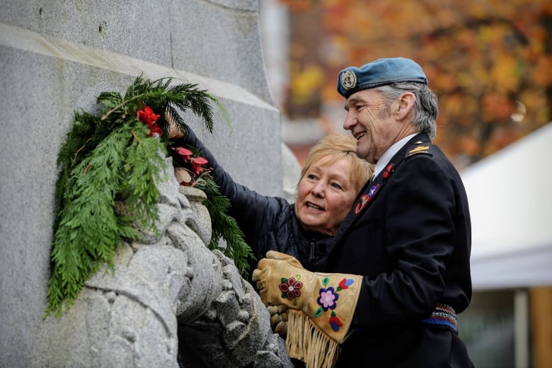 Two people, one in military uniform, adorn a cenotaph.