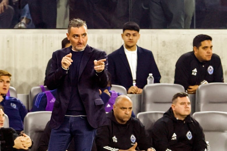 A soccer manager points to his left as other players sit behind him.