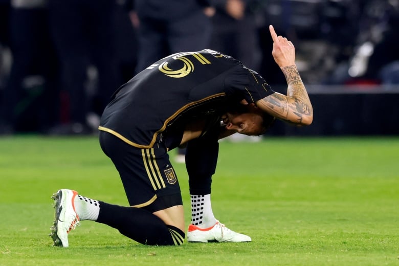 A soccer player raises his finger to the sky as he kneels to celebrate.