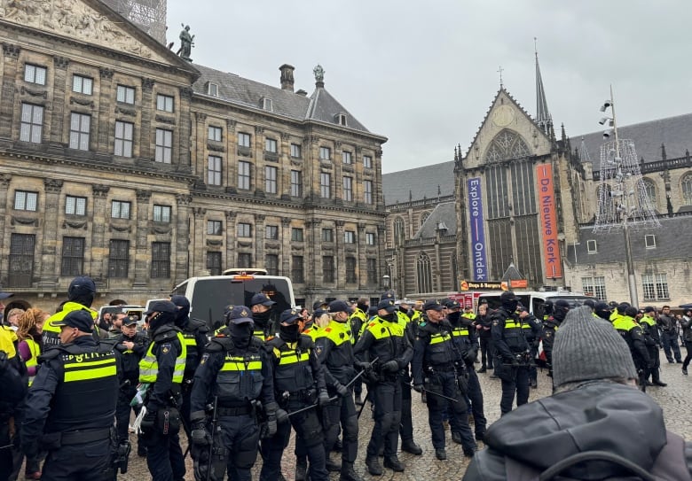 A line of police officers stands guard in a public square.