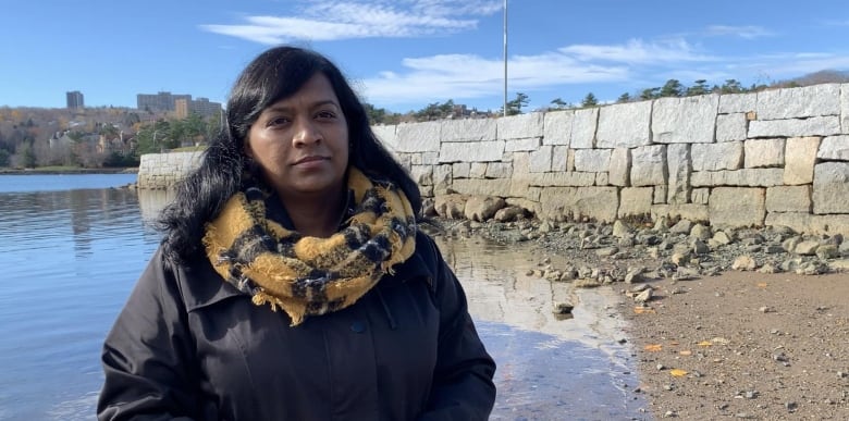 Woman looks at camera. Background is a calm blue ocean and a stone wall. 