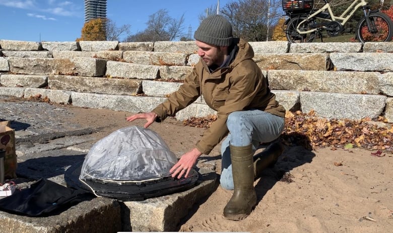 Man crouches necxt to a dome-like device. 