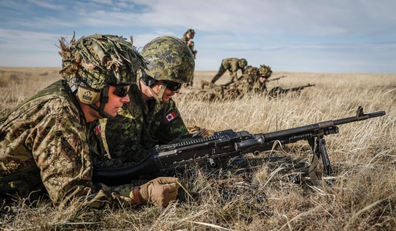 Two reservists lie in high grass with an automatic weapon during a training exercise.