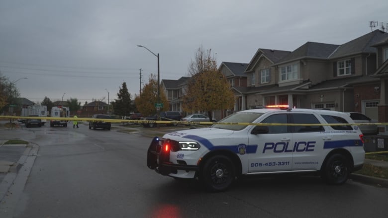 A police vehicle is seen behind yellow tape parked in front of a row of houses. 