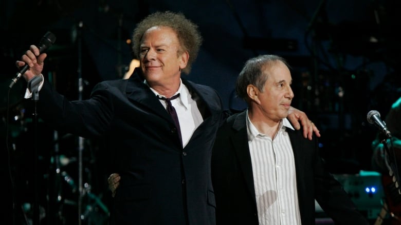 Two men stand on stage with an arm around each other.