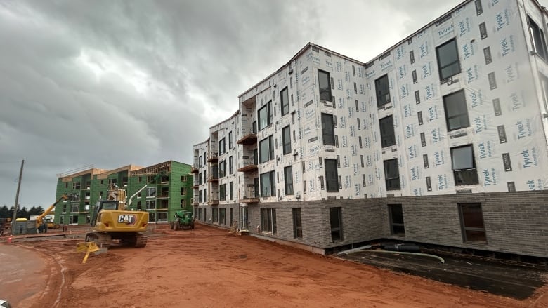 An apartment complex under construction with a backhoe on an unpaved lot.