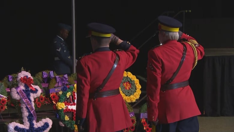 Two people wearing red salute in front of wreaths.