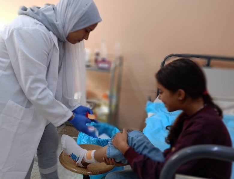 A woman treats a young girl sitting on a hospital bed.