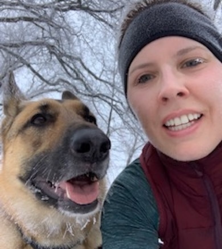 A woman stands with a dog in the winter.