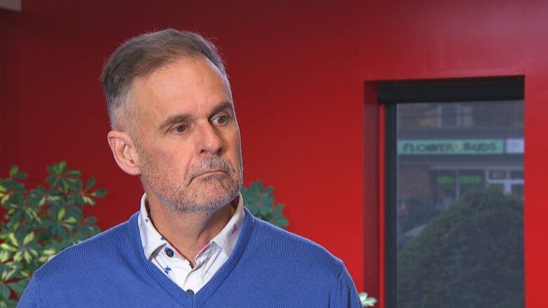 Man in blue sweater standing in front of red wall.