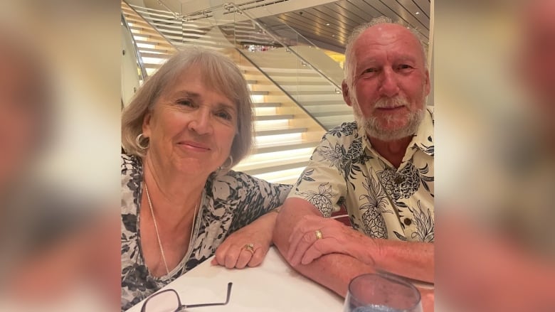 A couple in their 70s sitting for a photo in front of a set of stairs. 