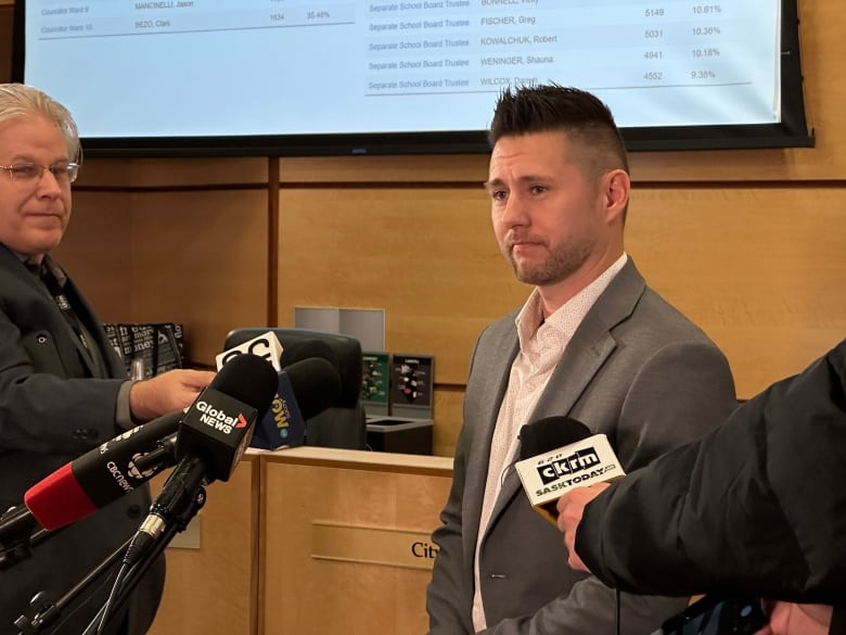 A man in a grey suit surrounded by microphones. 