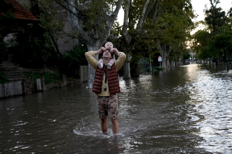 Man knee-deep in water holds baby on his shoulders