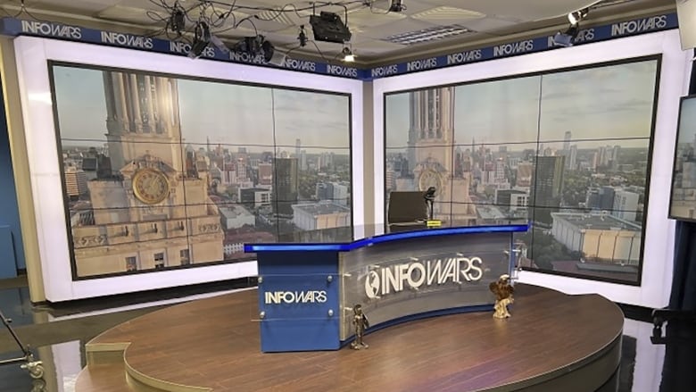 A television studio is shown with a long desk that says Infowars.