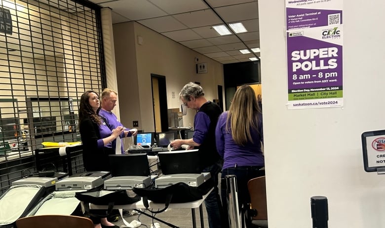 A group of people in purple shirts stand around electronic equipment.