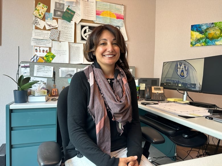 A woman sits smiling at a desk.