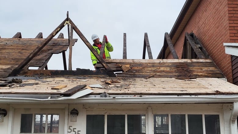 Man in hard hat stands amid the wood frame of an old house