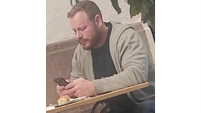 A bearded man looks down at a mobile phone.