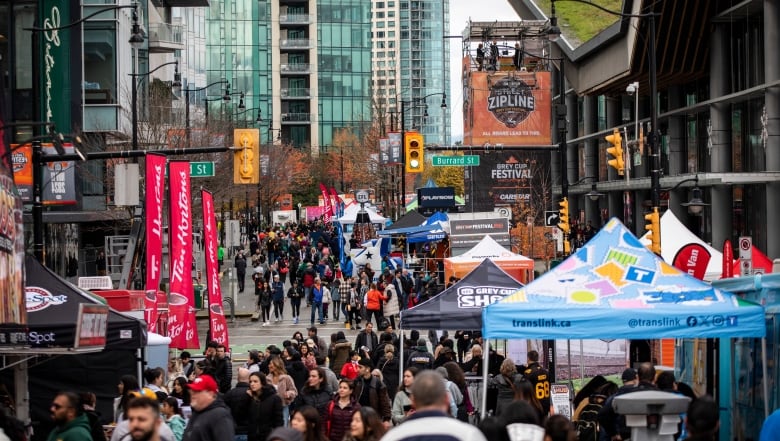 A large crowd of people are gathered on a city street, lined with tents and signage.