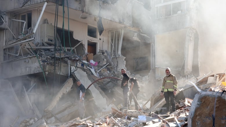 People stand on rubble as smoke rises.