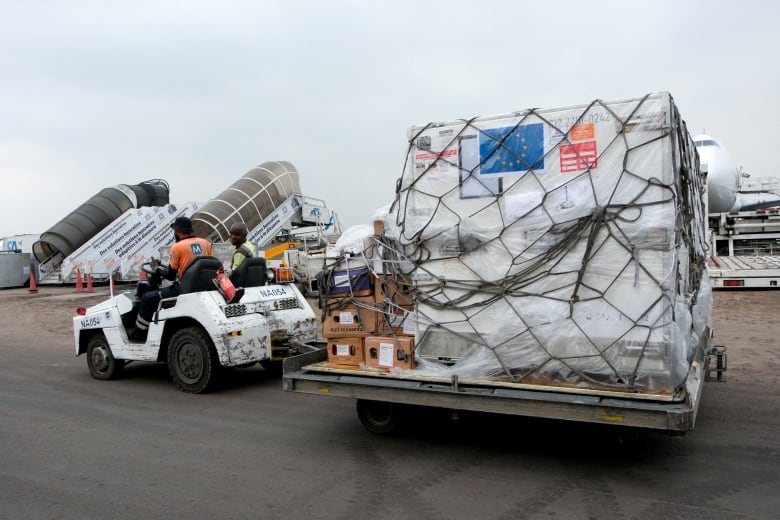 A large container is seen on the tarmac of an airport with a vehicle is hooked up to it to transport it.