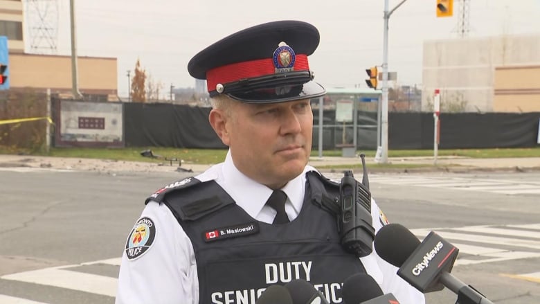 Police officer standing in front of an intersection where there is caution tape on the side and debris on the ground from a car crash