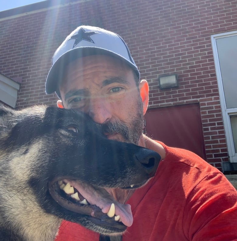 A man wearing a red t-shirt and baseball cap holding a dog. 