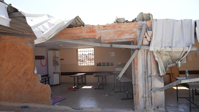 A destroyed building with some school furniture still standing inside.