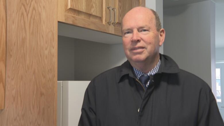 A man stands in a kitchen and smiles.