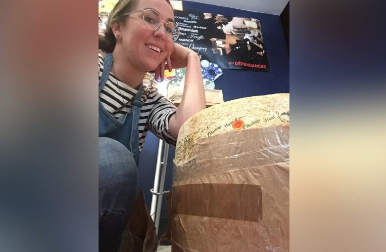 A woman poses with her elbow on a wheel of cheese.