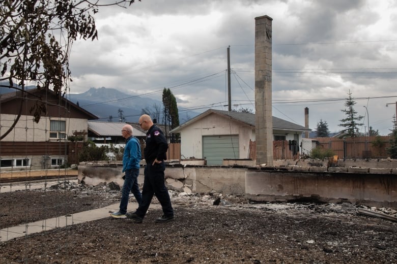 Two people are pictured walking through burnt debris.