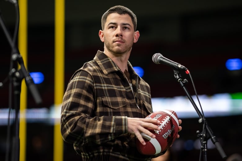 A man holds a football while staring off to the side. 