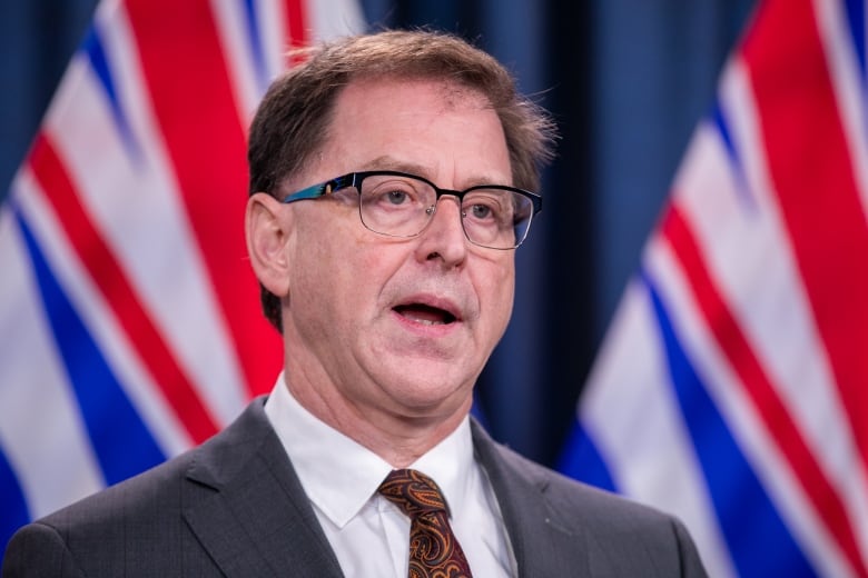 A man speaks in front of two B.C. flags.