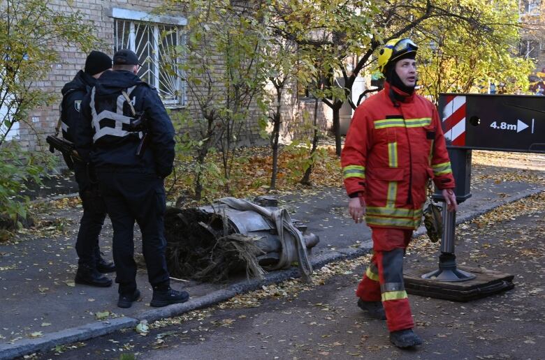 Police officers and other emergency workers gather around metal debris on laying on a sidewalk.