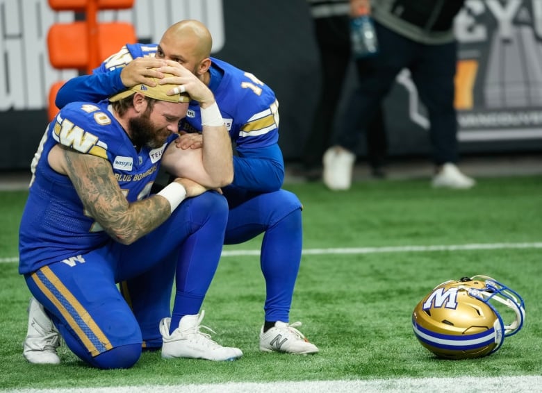 Two football players commiserate on the sidelines after a loss.