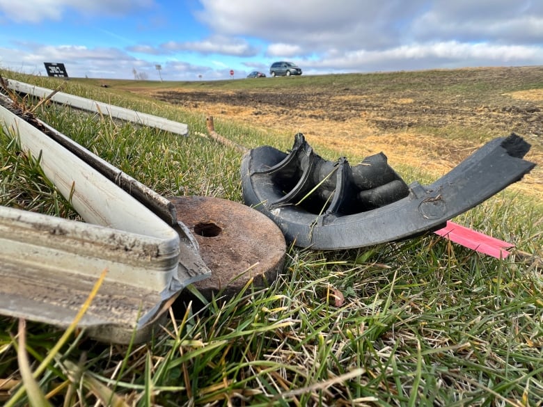 Pieces of a car lay on the grass at a highway intersection. 