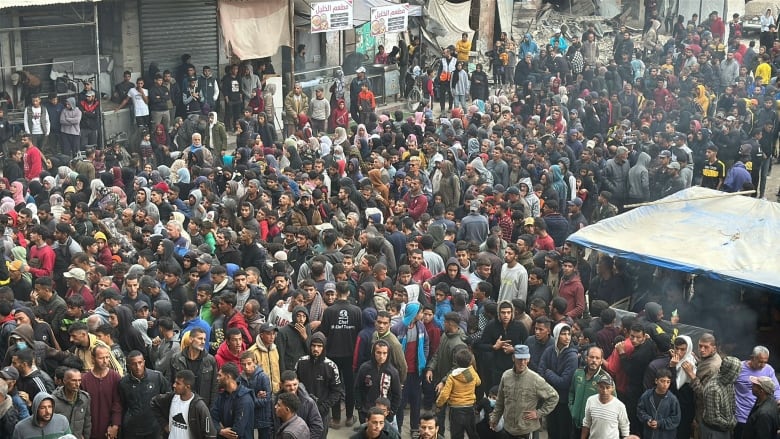 Dozens of people stand outside of a bakery.