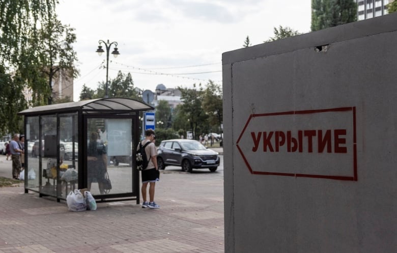 A bus shelter with people inside and a large concrete structure are both shown.