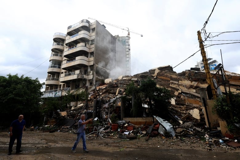 Two men walk past a flattened condo building.