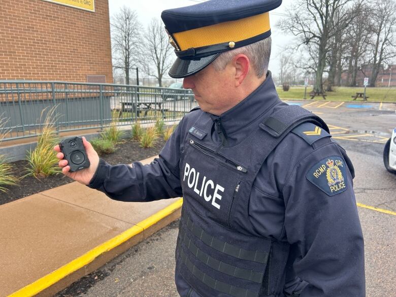 A male RCMP officer in uniform looking at a body camera in his hand.