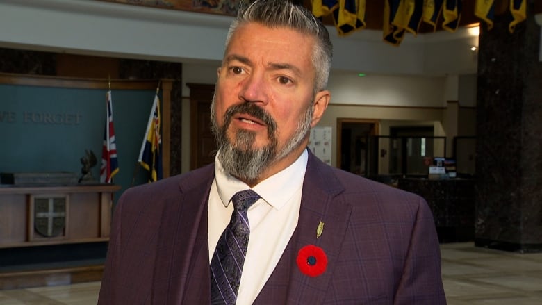 Man with short grey hair wearing a purple three piece suit.