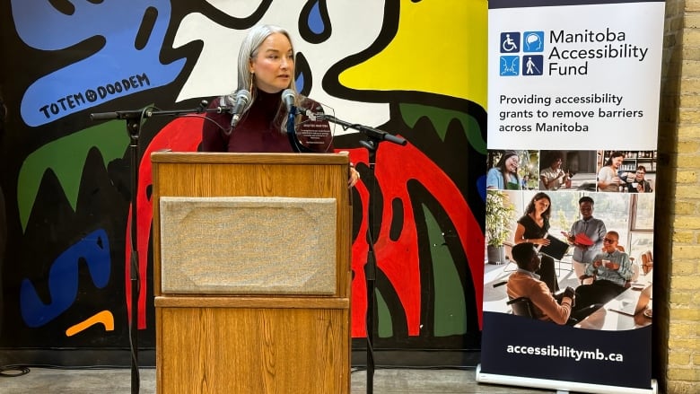 A woman stands in front of colourful artwork at a podium. 