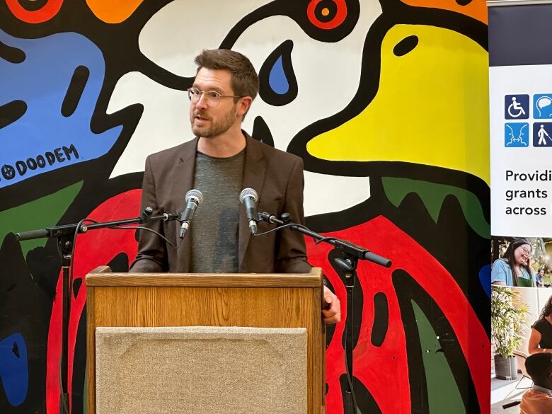 A man speaks at a podium in front of a colourful backdrop during a press conference. 