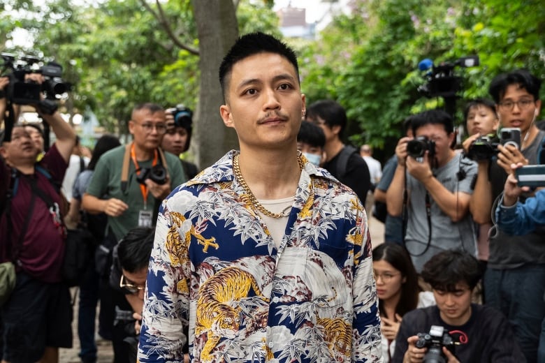 A man in a colourful, patterned shirt is surrounded by photographers. 