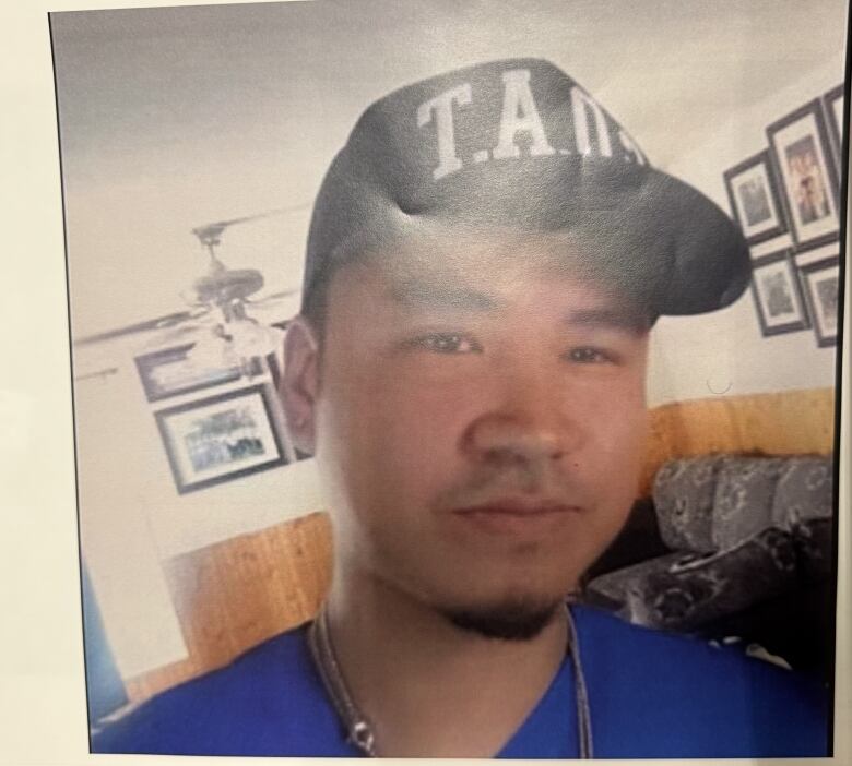 A young man is seen in a photograph wearing a baseball cap and a blue shirt 