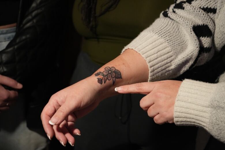 A woman holds out her arm to show off a tattoo she received at the Wahkotowin Tattoo Gathering, which is of a flower with two strawberries.