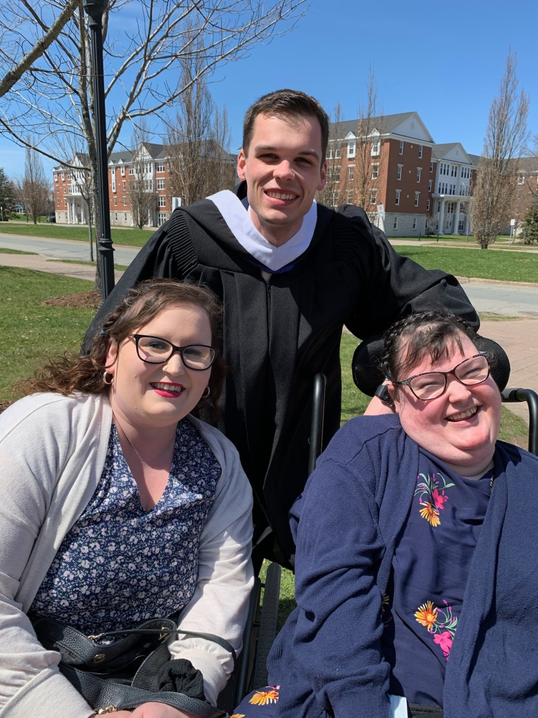 A man is shown between two women who are his sisters and all are smiling for the camera.