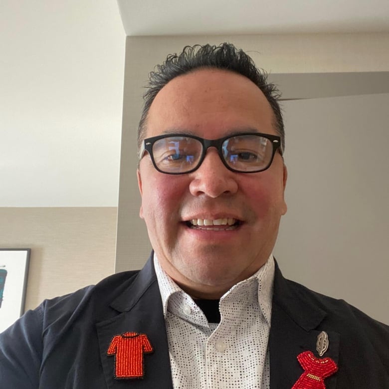 A man with glasses wearing a dark jacket with two orange pins on it.